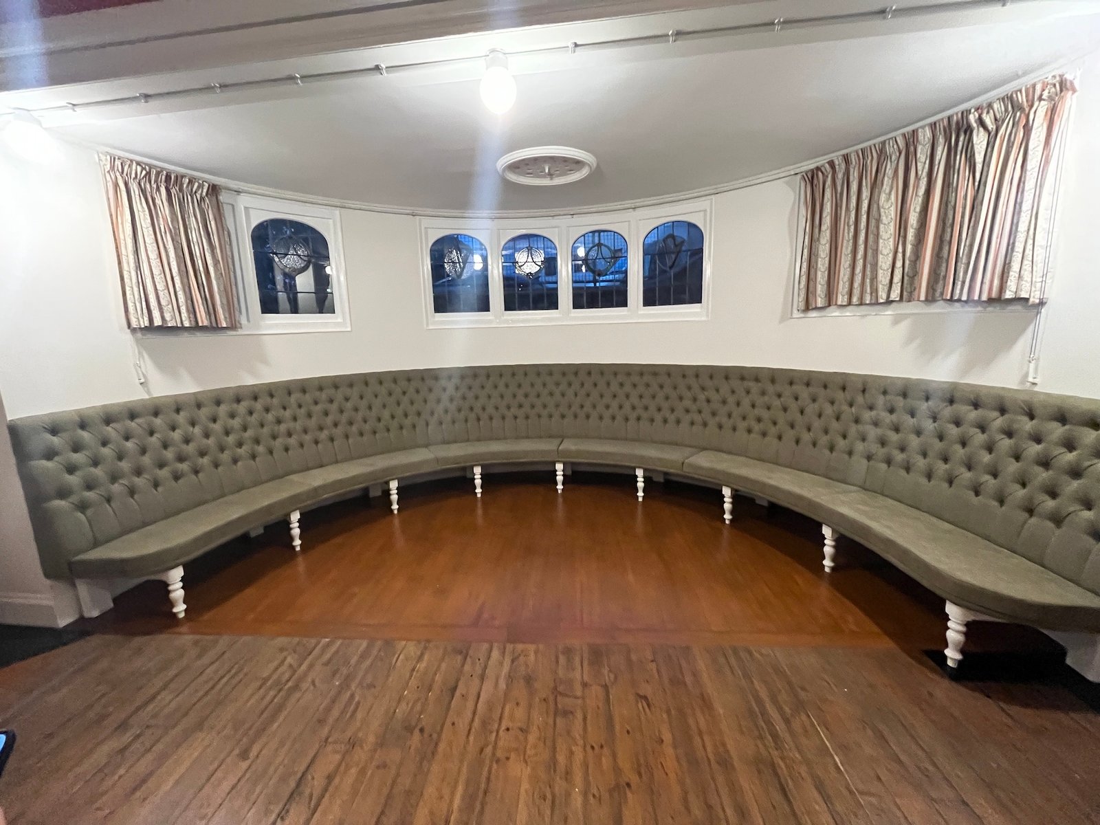 Large curved grey buttoned banquette under arched windows